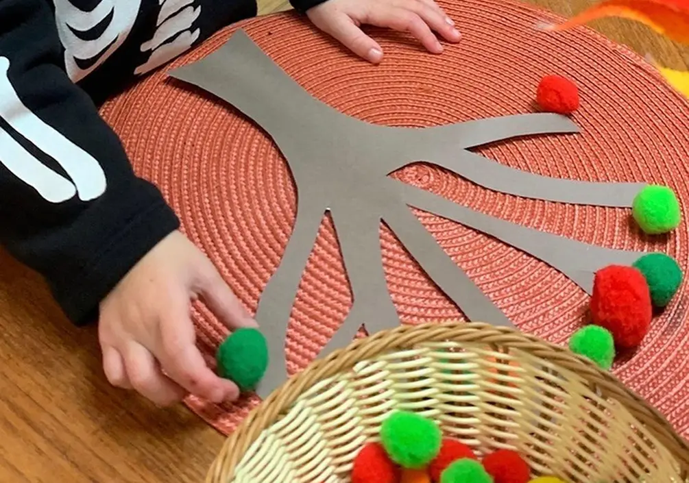Child creating a tree craft with colourful pom-poms at Learning Together Childcare
