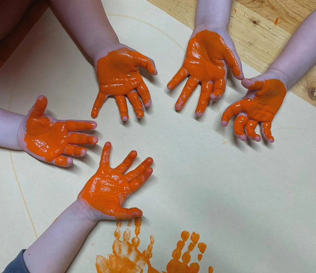 Children making orange handprints during a group painting activity at Learning Together Childcare