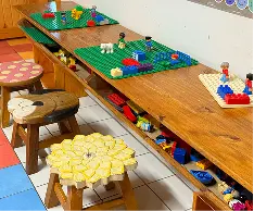 Childcare classroom with wooden activity tables set up with colourful learning materials and crafts.